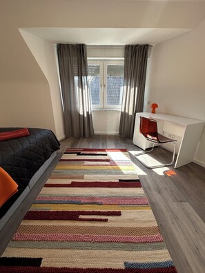 Une chambre à coucher avec un lit, un bureau et une fenêtre avec des rideaux.