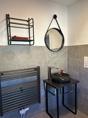 Une salle de bain équipée d’un porte-serviettes, d’un miroir rond, d’un lavabo avec un bac et d’un radiateur.