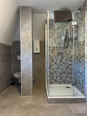 A bathroom with a glass shower enclosure, a toilet, and a towel rack.
