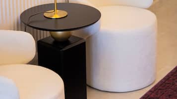 Un interior moderno con una mesa redonda negra, una lámpara dorada y asientos con cojines blancos.