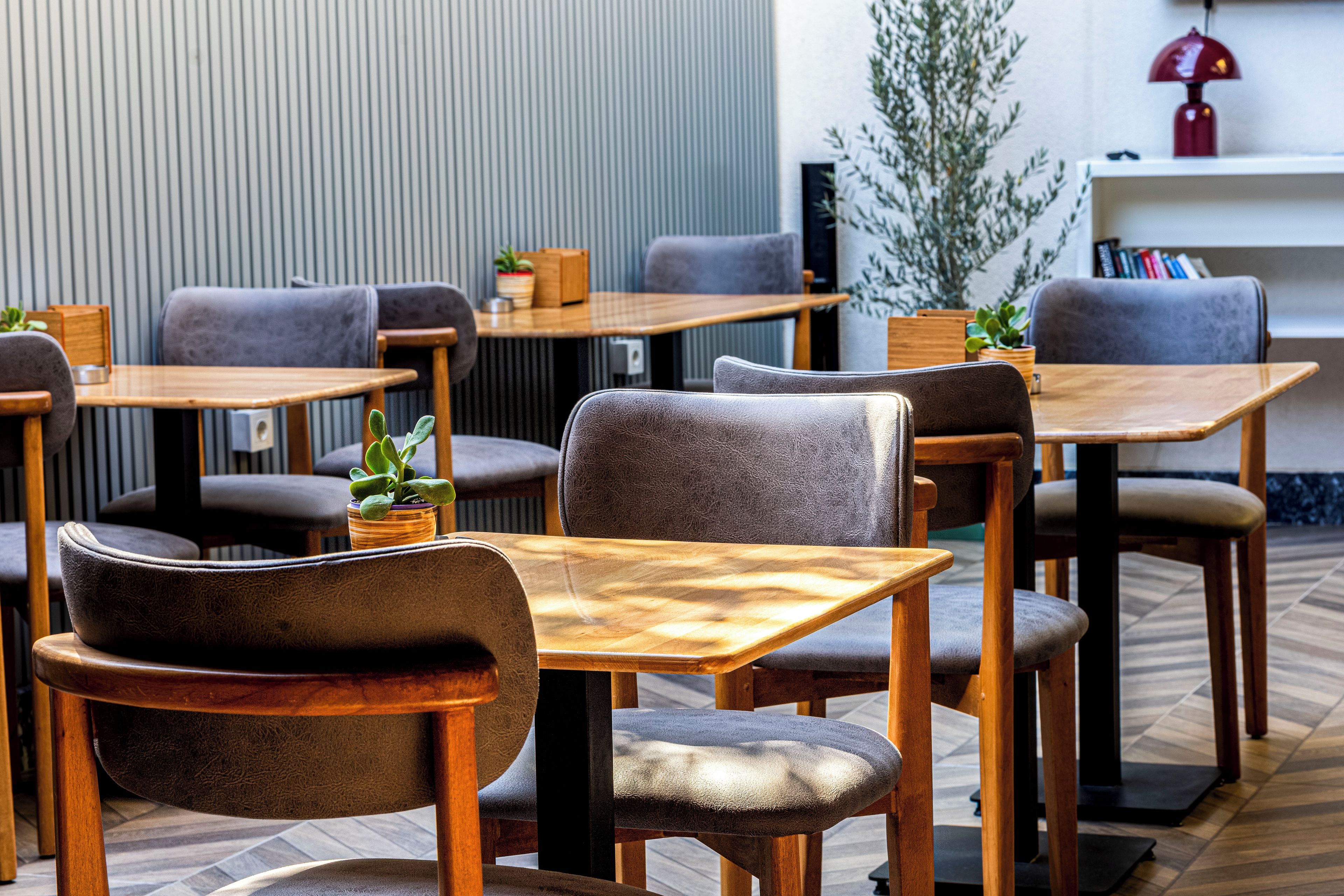 Un área de estar interior moderna con mesas de madera y sillas tapizadas en gris.