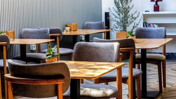 Un área de estar interior moderna con mesas de madera y sillas tapizadas en gris.