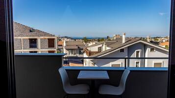 Un balcón con dos sillas blancas y una mesita, con vistas a una zona residencial con varios edificios y un cielo despejado.