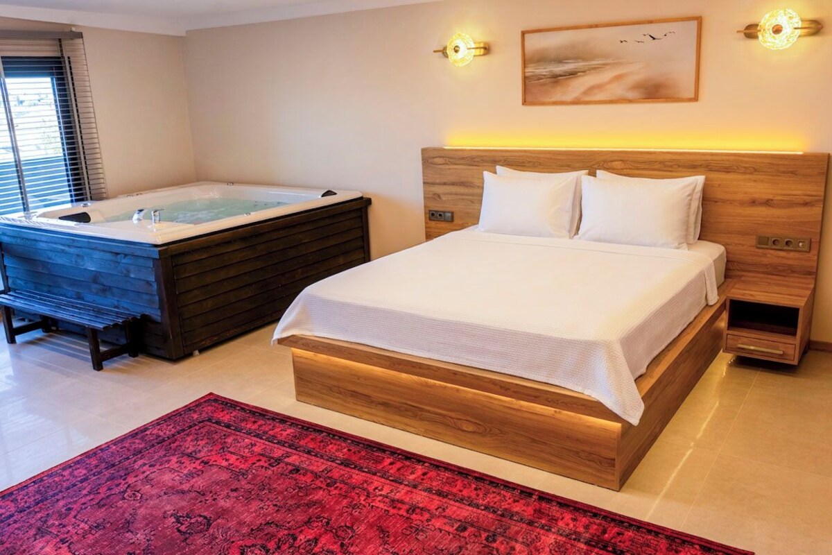 A bedroom with a wooden headboard, a large bed, a red rug, and a hot tub.