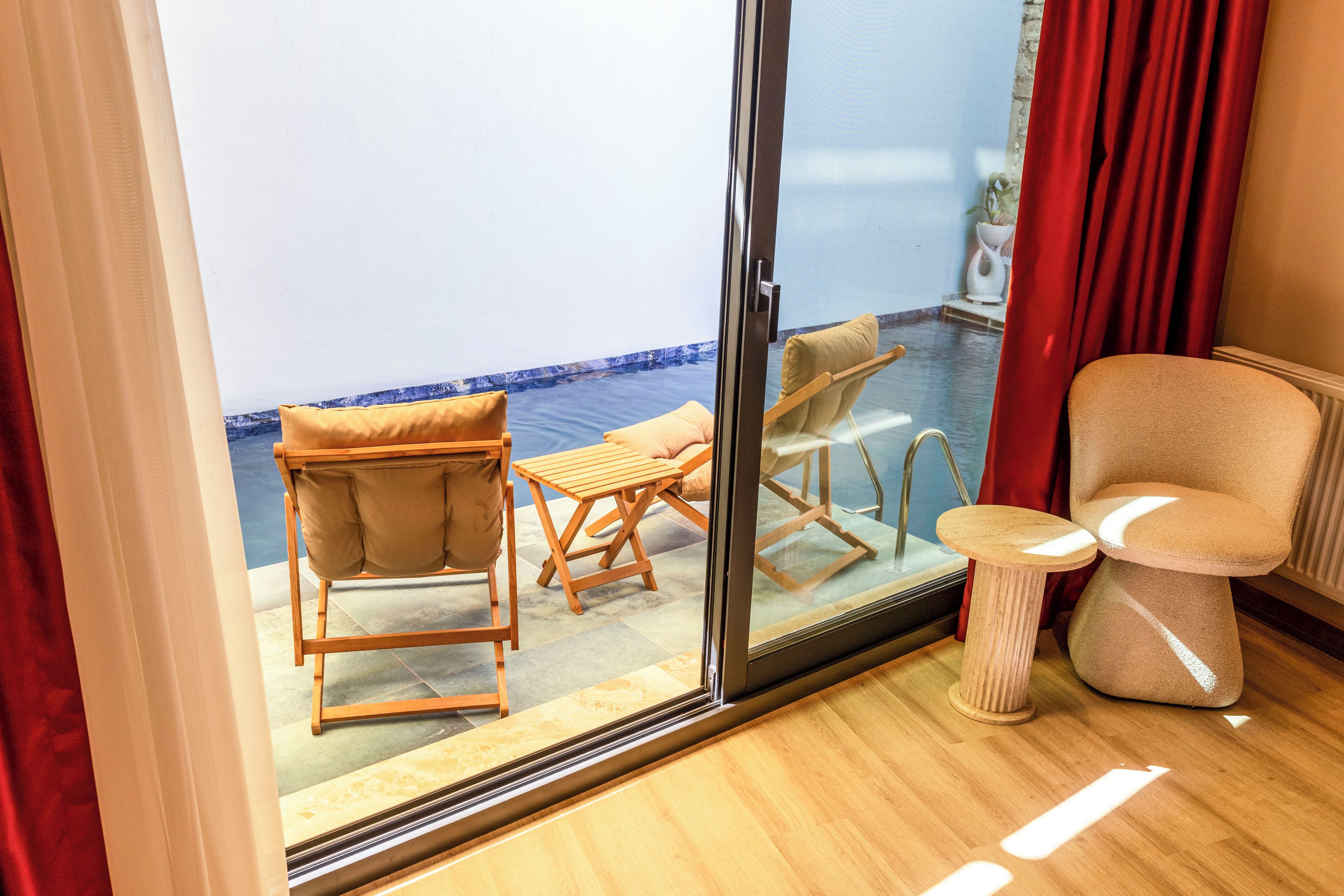 Habitación con puerta de vidrio corredera que da a un balcón con piscina, muebles de madera y una pequeña mesa.