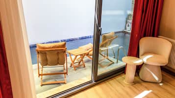 Habitación con puerta de vidrio corredera que da a un balcón con piscina, muebles de madera y una pequeña mesa.