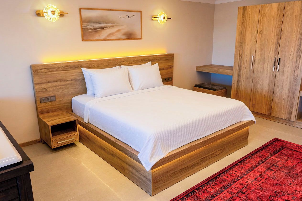 A large bed with a wooden headboard, bedside tables, a red rug, and a wardrobe.