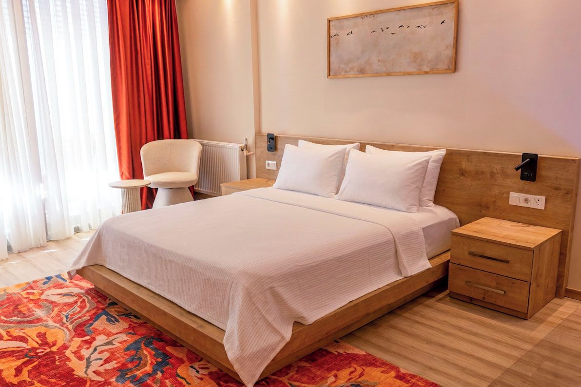 Una habitación de hotel con cama, mesitas de noche, una silla, un radiador y un cuadro en la pared.