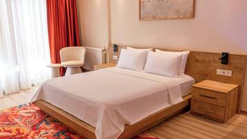 Una habitación de hotel con cama, mesitas de noche, una silla, un radiador y un cuadro en la pared.