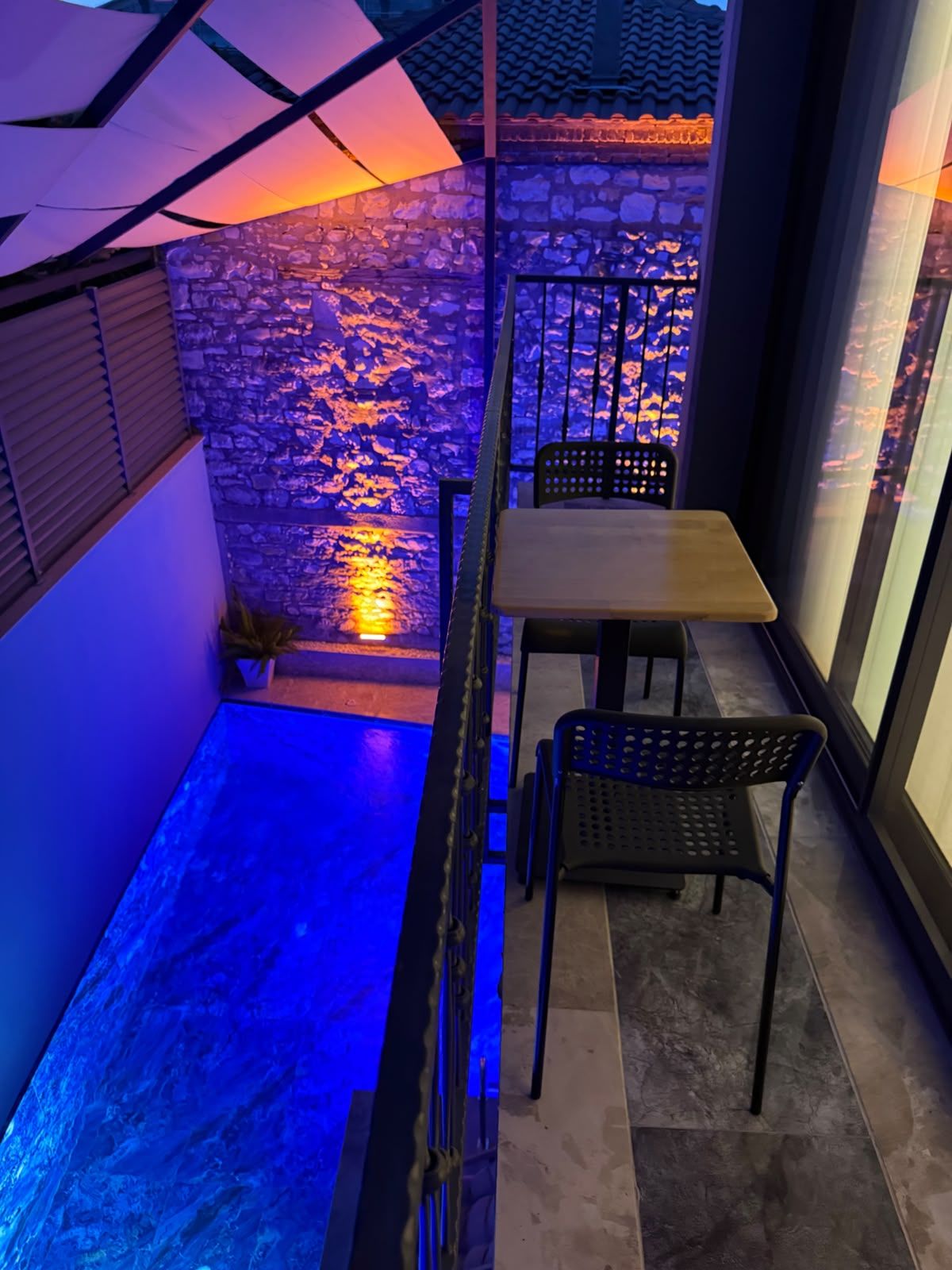 Un espacio exterior reducido con una pared de piedra, una mesa pequeña y dos sillas.