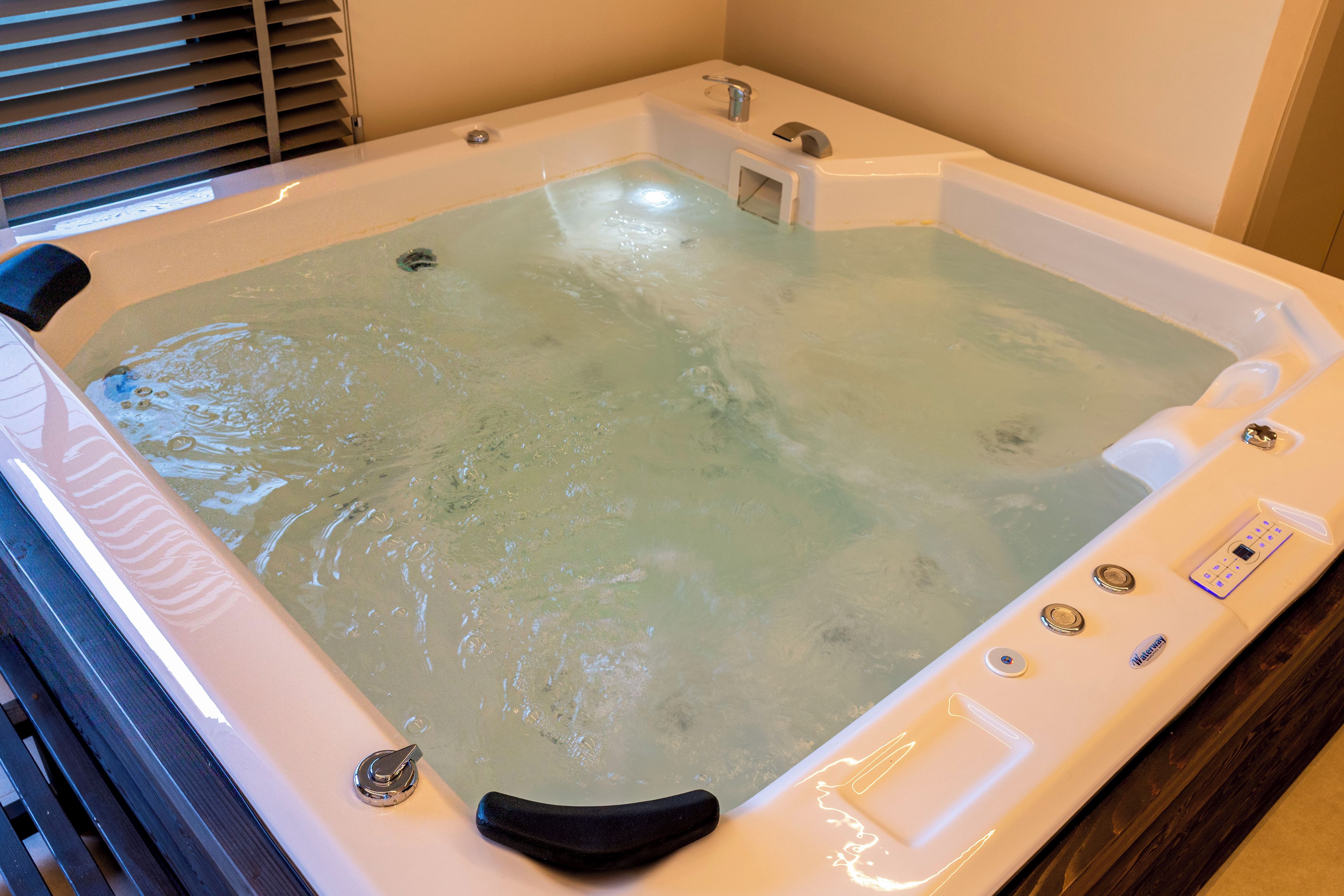 Un jacuzzi con panel de control, un asiento integrado y un ventanal.