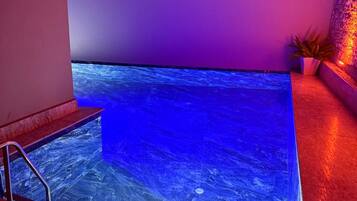 Una piscina con fondo de cristal, rodeada de paredes rojas y una planta en maceta.