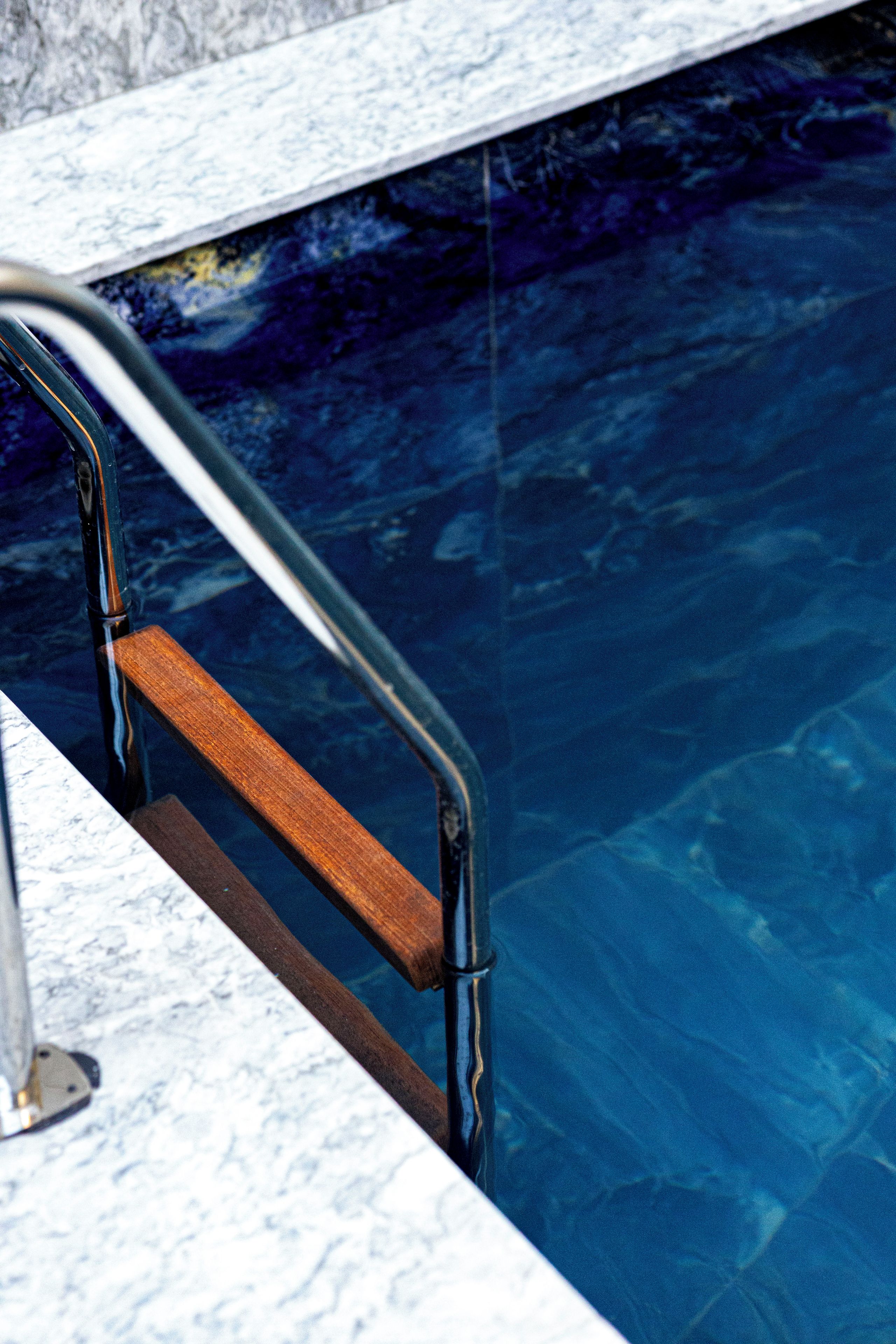 A poolside area with a marble edge and a wooden handrail.