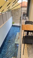 Un espacio pequeño con piscina al aire libre, una pared de piedra, una mesa de madera y sillas negras.