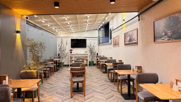 Un restaurante con mesas y sillas de madera, un piso con patrón de espiga y un televisor montado en la pared.