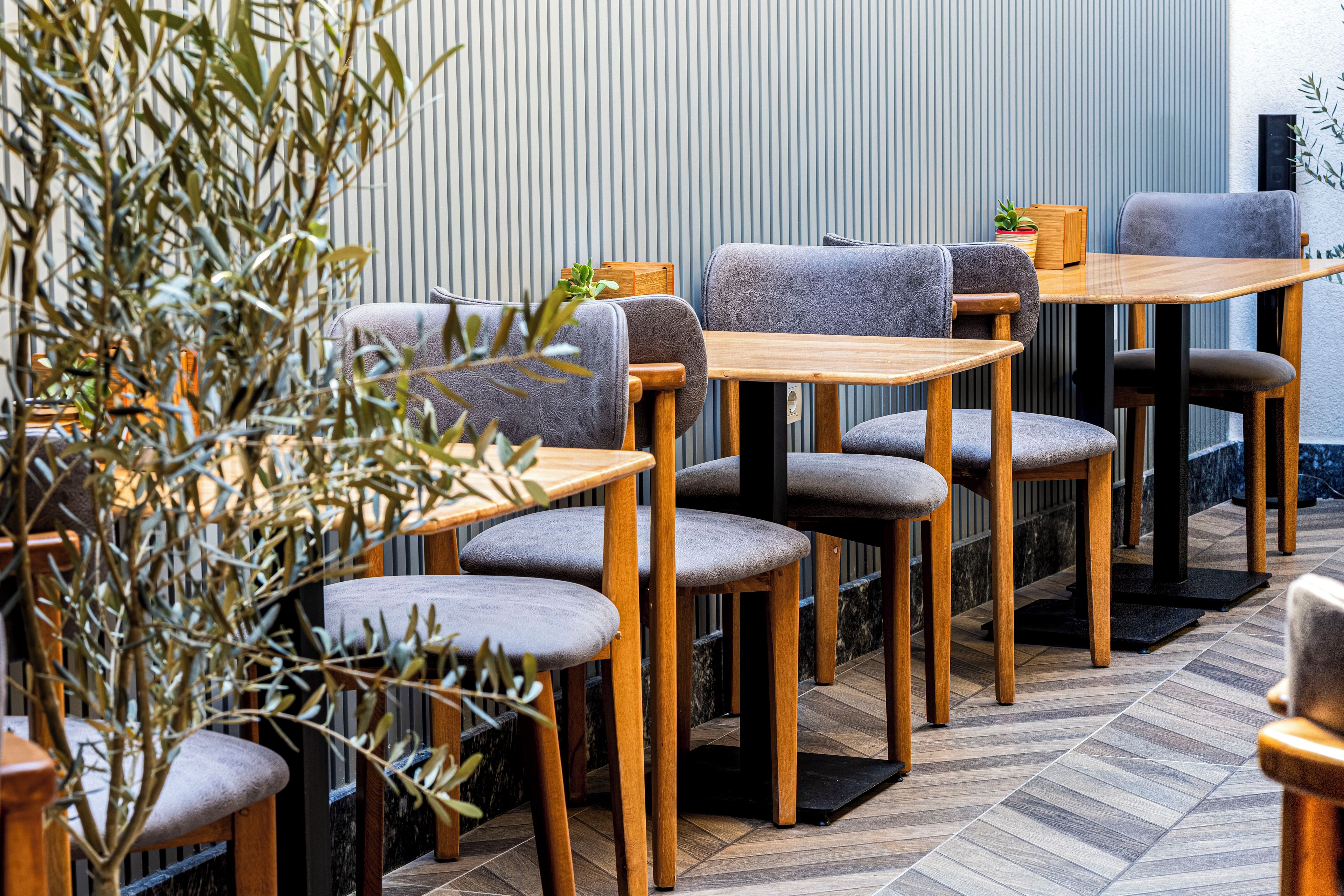 Interior de restaurante con mesas y sillas de madera, una planta en maceta y una pared a rayas.