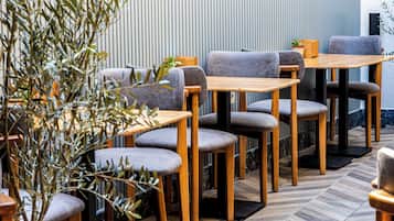 Interior de restaurante con mesas y sillas de madera, una planta en maceta y una pared a rayas.