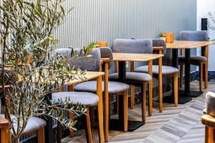 Interior de restaurante con mesas y sillas de madera, una planta en maceta y una pared a rayas.