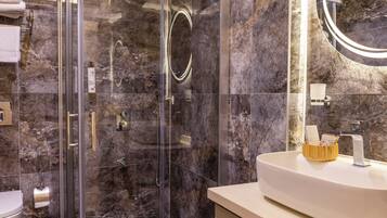 Un baño moderno con ducha de vidrio, paredes de mármol y lavamanos blanco con un cuenco de madera.