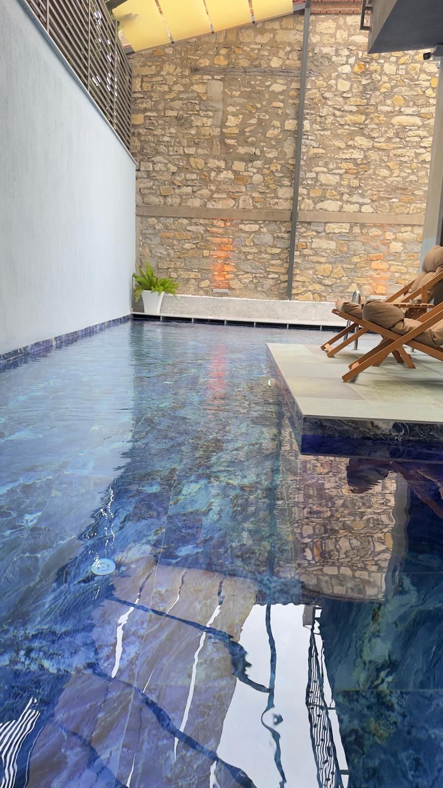Una piscina interior con pared de piedra y zona de descanso con una silla.