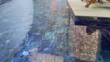 Una piscina interior con pared de piedra y zona de descanso con una silla.