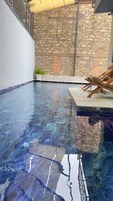 Una piscina interior con pared de piedra y zona de descanso con una silla.