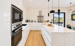 A modern kitchen with a built-in oven, a stove, and a large island with a marble countertop. - Contemporary Villa with Private Pool, Sleeps 6, 3 Bedrooms, Near Bonifacio/Porto Vecchio (FIGARI)