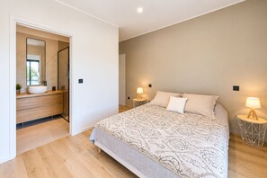 A bedroom with a bed, bedside lamps, a nightstand, a mirror, and a bathroom with a sink and mirror. - Contemporary Villa with Private Pool, Sleeps 6, 3 Bedrooms, Near Bonifacio/Porto Vecchio (FIGARI)