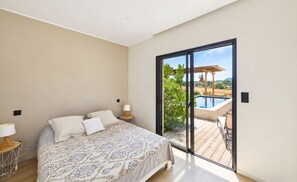 A bedroom with a large bed, a nightstand, a lamp, and a view of an outdoor swimming pool and patio area. - Contemporary Villa with Private Pool, Sleeps 6, 3 Bedrooms, Near Bonifacio/Porto Vecchio (FIGARI)