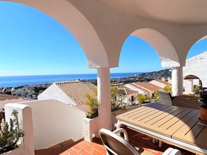 A terrace with a table and chairs, overlooking a coastal town and the sea. - Apartment in Nerja With Sea Views & Pool (Nerja)