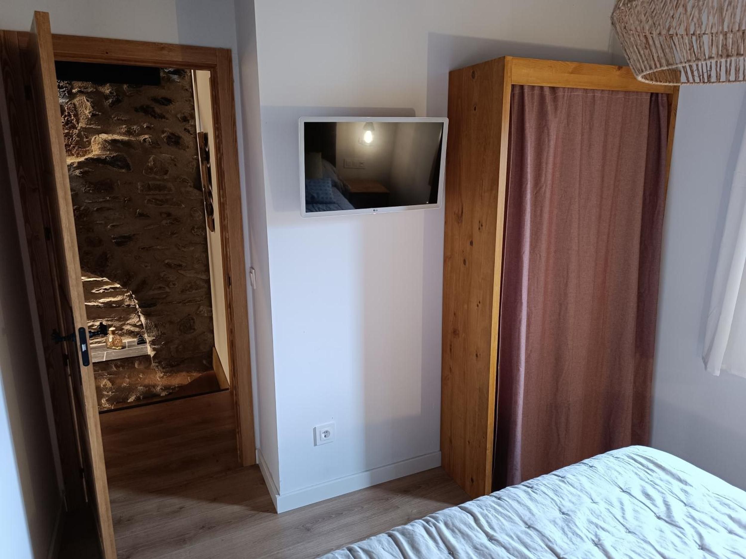 Une chambre à coucher avec un lit, une télévision, une armoire en bois et un mur en pierre.