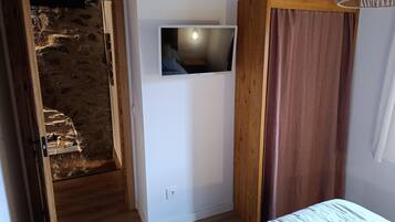 Une chambre à coucher avec un lit, une télévision, une armoire en bois et un mur en pierre.