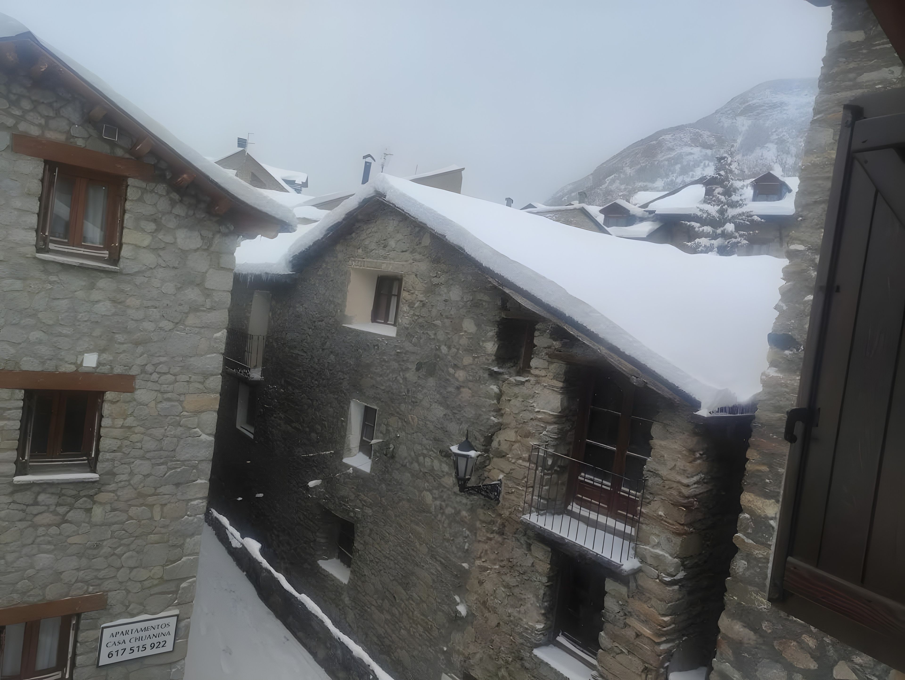 A stone building with multiple windows and balconies, surrounded by snow-covered terrain and mountains.