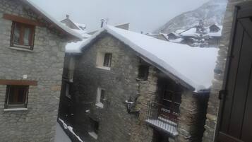 A stone building with multiple windows and balconies, surrounded by snow-covered terrain and mountains.
