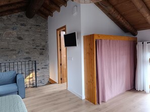 Habitació amb paret de pedra, sostre de fusta, televisió penjada a la paret i porta de fusta.