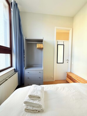 Een slaapkamer met een bed, een kast, een radiator en een deur met een spiegel.