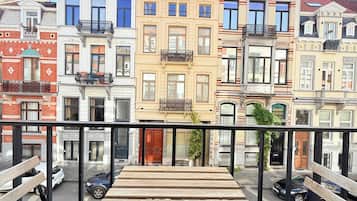 A balcony with a wooden table and benches, overlooking a row of colorful buildings with balconies.
