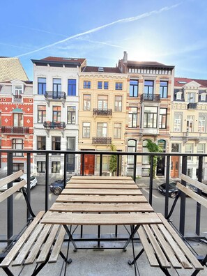 Een balkon met een houten tafel en bankjes, met uitzicht op een rij kleurrijke gebouwen met balkons.