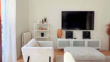 Een moderne woonkamer met een grote flatscreen televisie, witte banken, een witte kast en een radiator.