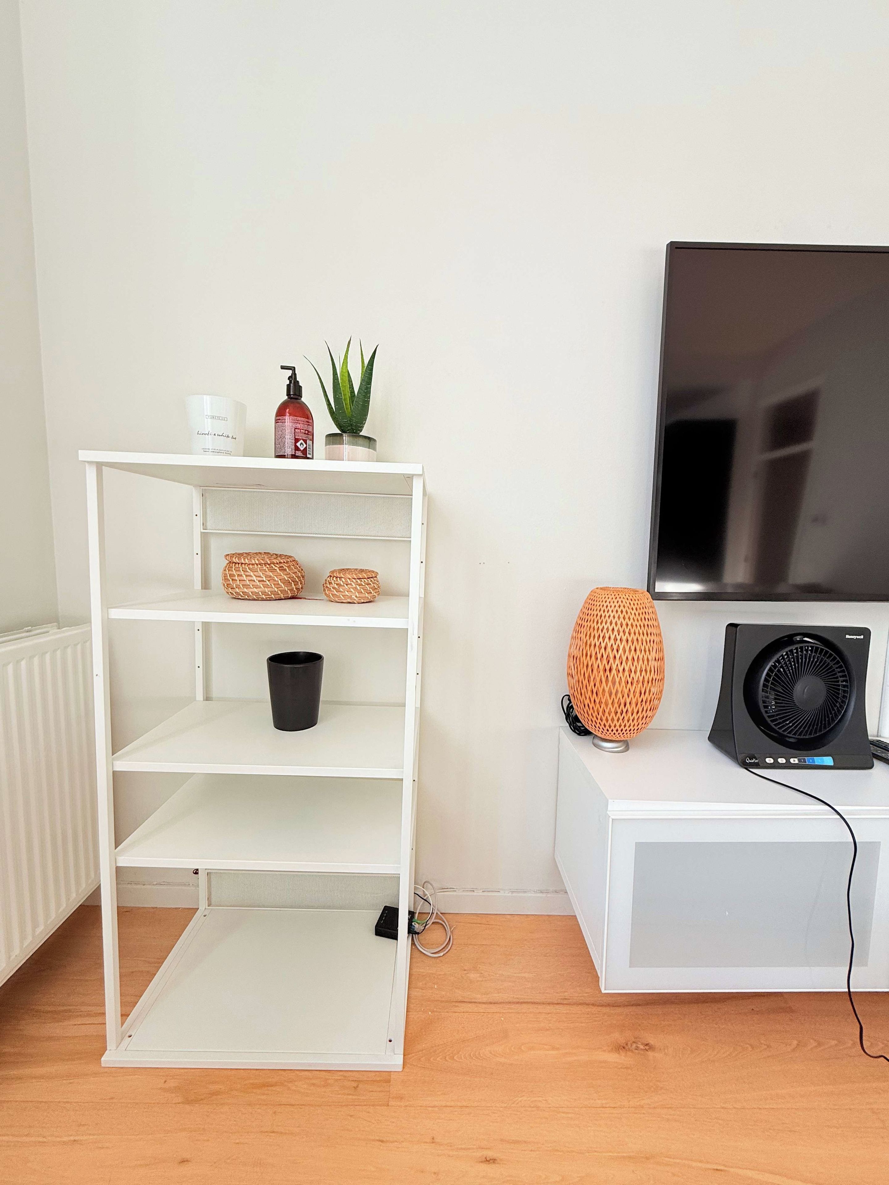 A white shelving unit with baskets, a black bucket, and a potted plant.