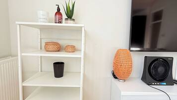 A white shelving unit with baskets, a black bucket, and a potted plant.