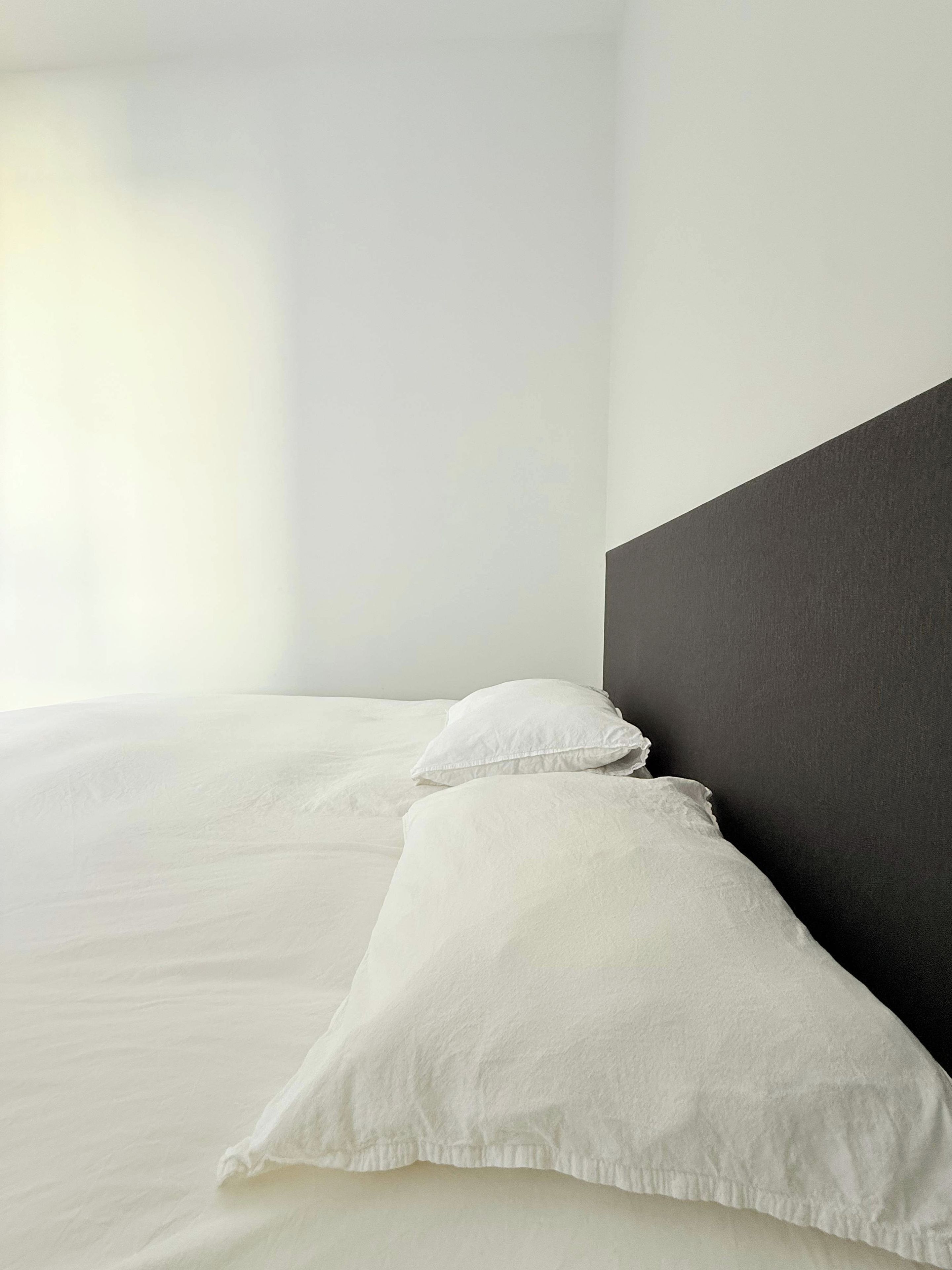 A bed with white bedding and pillows, a dark headboard, and a plain wall.