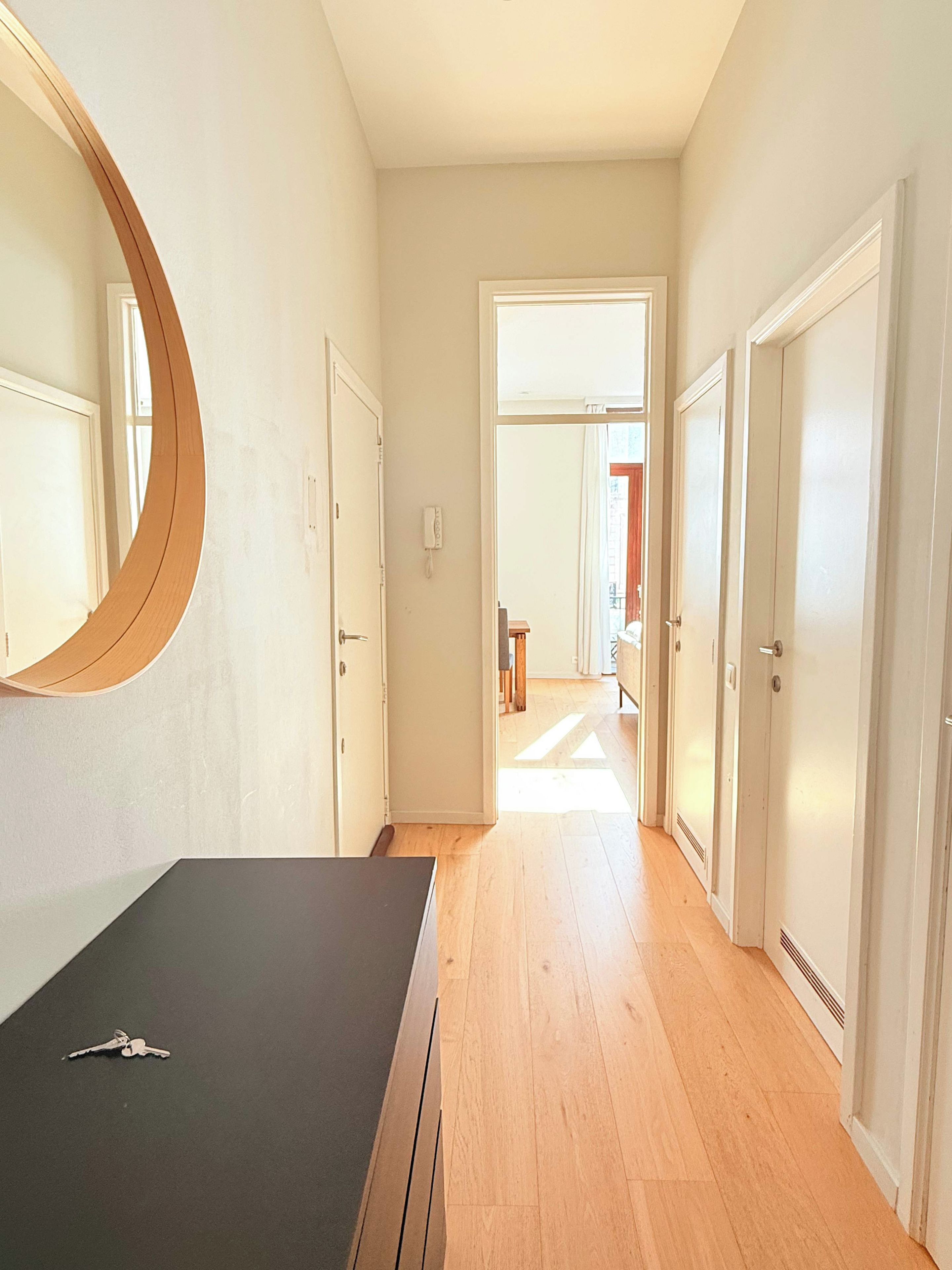 A hallway with a mirror, a desk, and a door leading to another room.