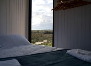 Un dormitorio con cama, vistas a un viñedo y un banco de madera en el exterior.