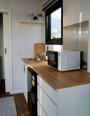 A compact kitchen with a wooden countertop, a built-in microwave, a sink, and a window with a view.