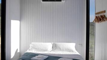A bedroom with a bed, white walls, a window, and an air conditioning unit.