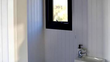 A small, enclosed bathroom with a toilet, a sink, and a window.