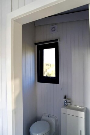 Un baño pequeño y cerrado con inodoro, lavamanos y ventana.