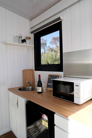 Una cucina compatta con lavandino, forno a microonde e tagliere in legno.