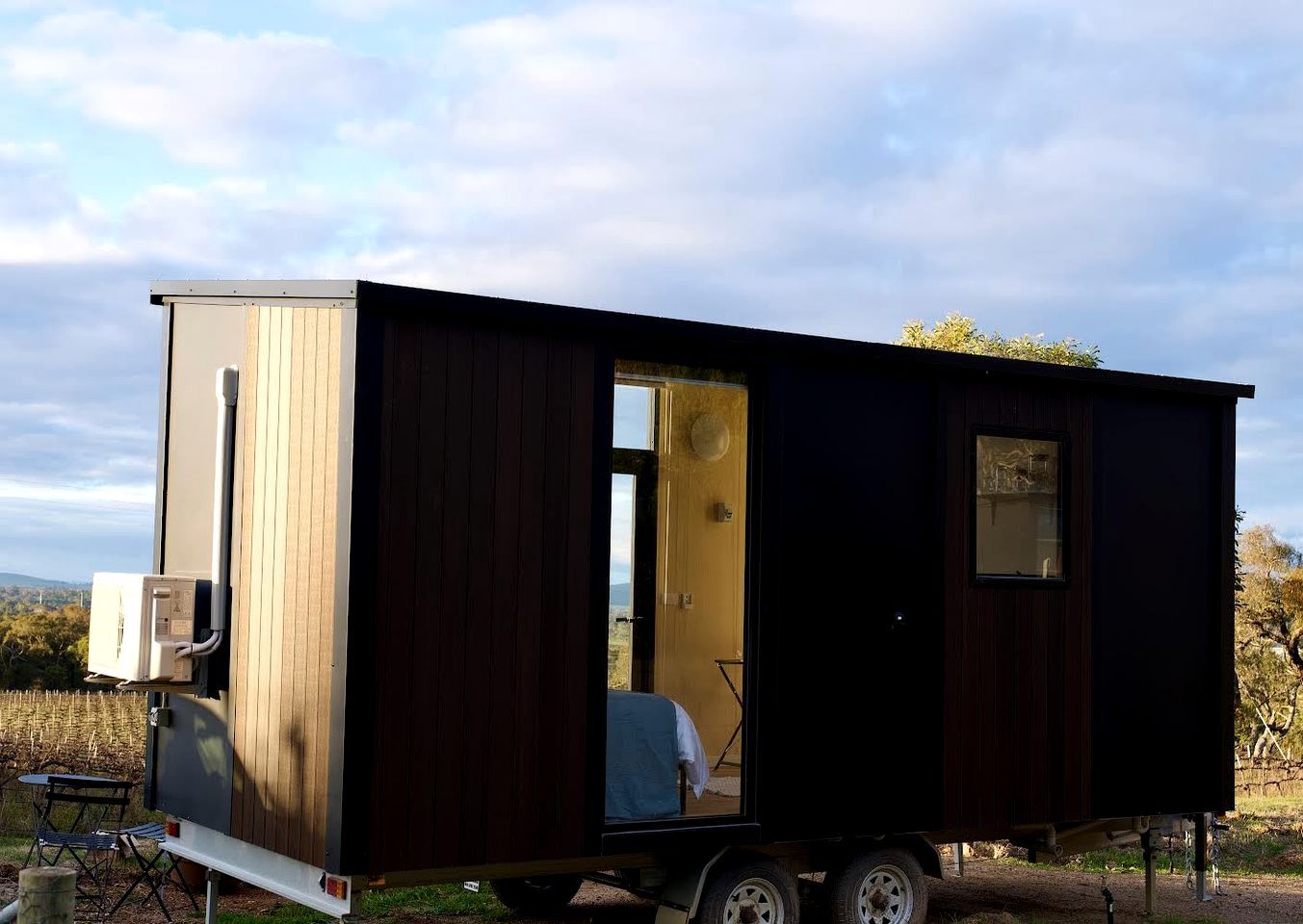 A mobile home with a large window, a door, and a small table with chairs.